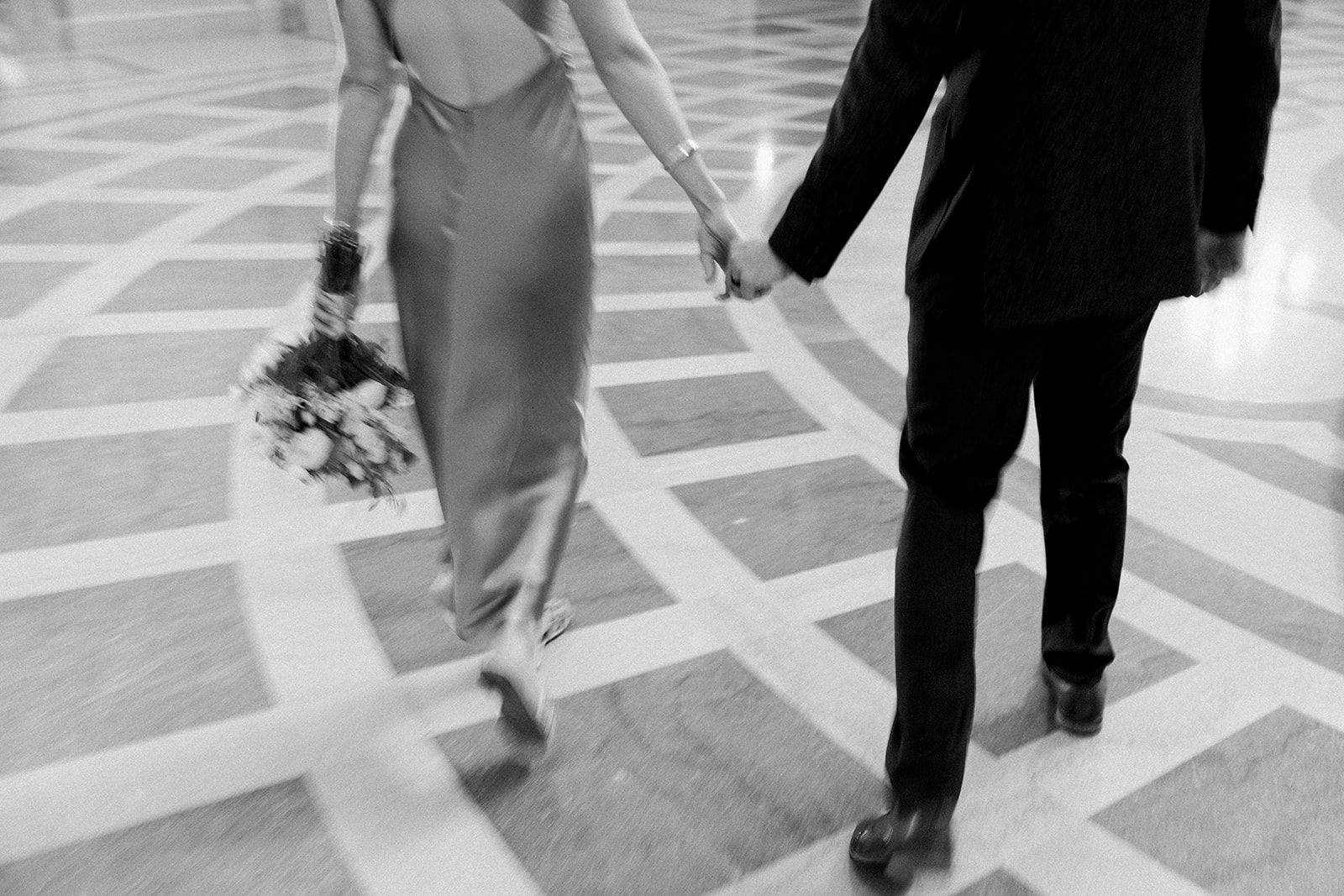 black and white blurry photo of bride and groom holding hands and walking away
